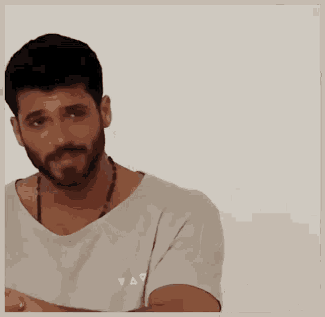 a man with a beard is wearing a white t-shirt and a necklace
