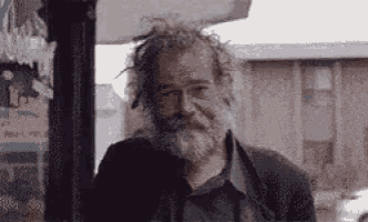 a homeless man with glasses and a beard is standing in front of a building .
