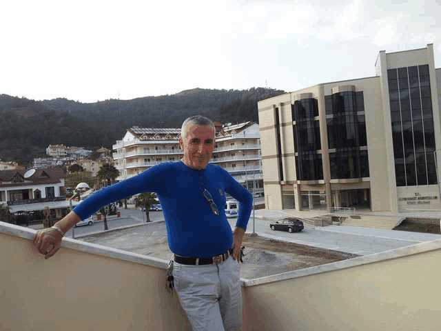 a man in a blue shirt stands on a balcony in front of a building that says ' tc ' on it