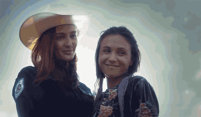 a woman in a cowboy hat stands next to another woman in a black dress