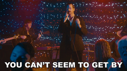 a man singing into a microphone with the words " you can 't seem to get by " above him