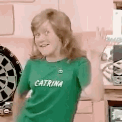 a woman wearing a green shirt that says caterina is standing in front of a dartboard .