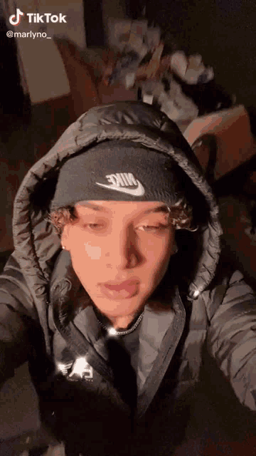 a young man wearing a hooded jacket and a black beanie is taking a selfie .