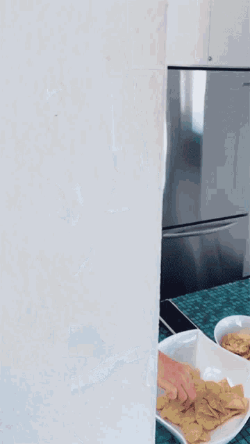 a person reaches into a bowl of chips in front of a refrigerator