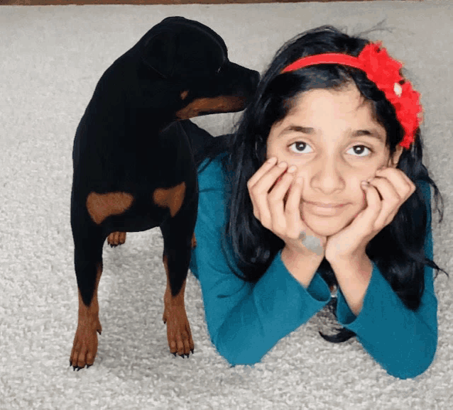 a girl with a red headband is laying on the floor next to a small black dog