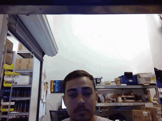 a man with a beard is looking at the camera in a room with boxes on shelves