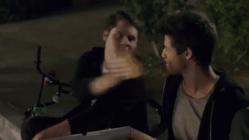 two young men are eating a slice of pizza together .