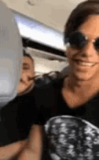 a woman wearing sunglasses is smiling while sitting on a plane .