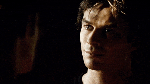 a man with a serious look on his face stands next to another man in a dark room