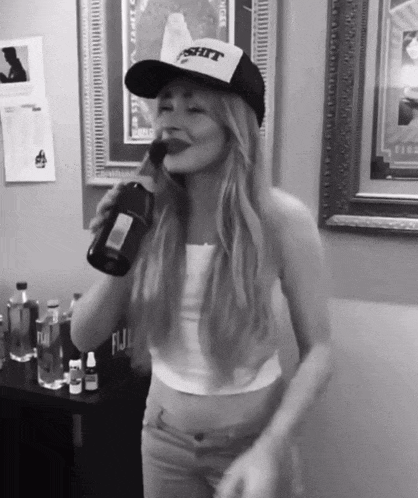 a woman wearing a hat that says " shit " drinks from a bottle