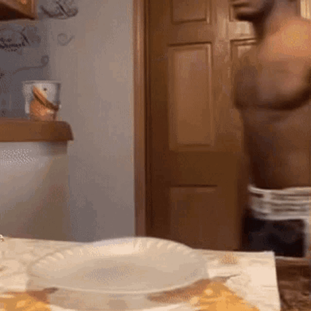 a man without a shirt is standing in front of a table with a paper plate on it