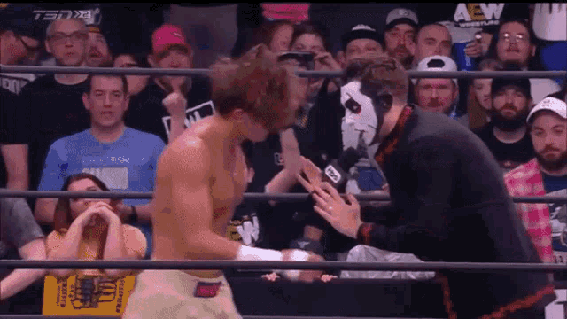 a man in a wrestling ring is talking to another man in front of a crowd that is watching a wrestling match .
