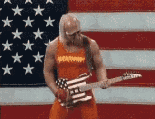 a man in an orange tank top is playing a guitar in front of a large american flag .