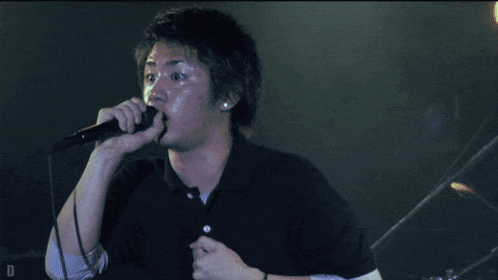a man singing into a microphone with the letter d visible behind him