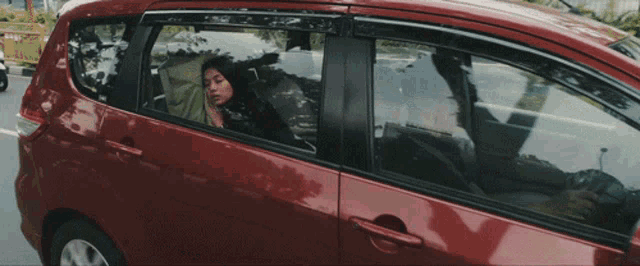 a woman is sitting in a red car talking on a cell phone