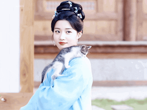 a woman in a blue dress is holding a small cat on her shoulder