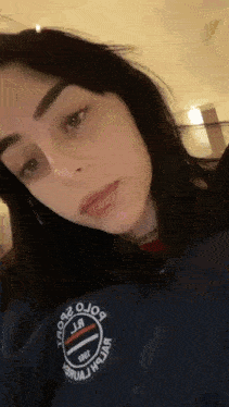 a close up of a woman 's face wearing a blue jacket with a sticker on it .