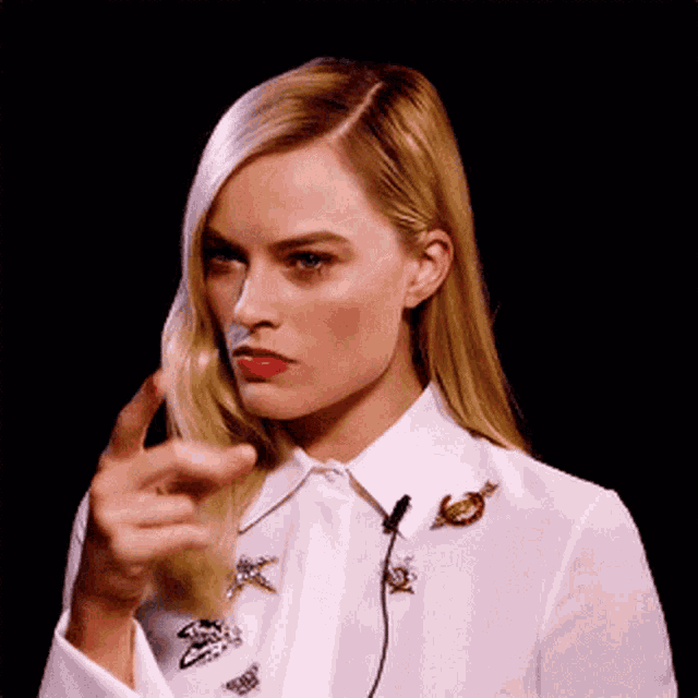 a woman in a white shirt is pointing her finger at the camera