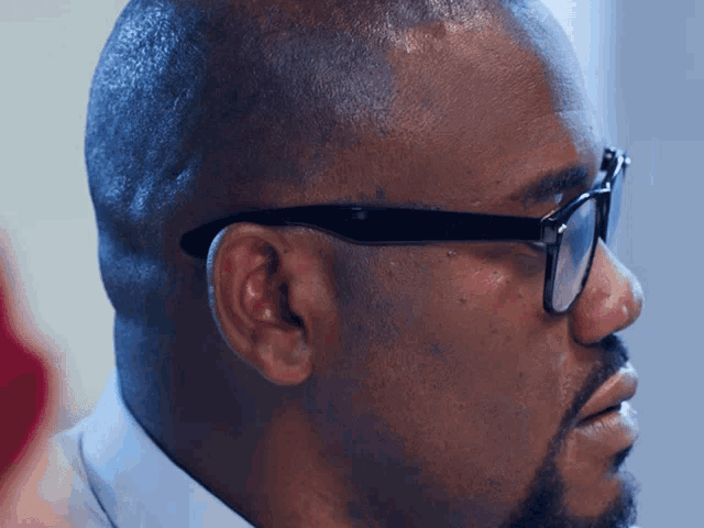 a man wearing glasses and a blue shirt is looking to the side