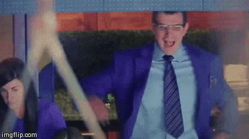 a man in a purple suit and tie is dancing with a woman in a blue shirt behind him .
