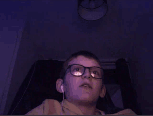 a young boy wearing glasses and ear buds looks up at something
