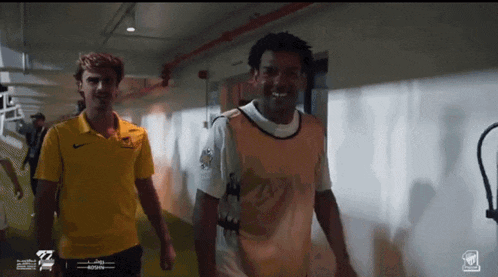 a man in a yellow nike shirt walks down a hallway with another man