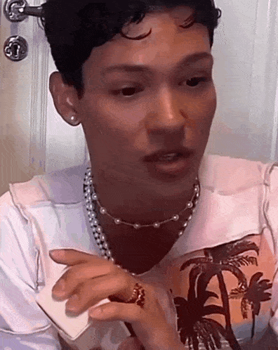 a man wearing a pearl necklace and a ring is talking on a phone .