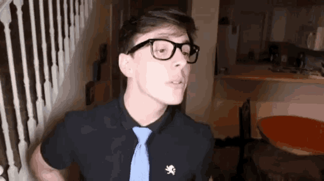 a young man wearing glasses , a black shirt and a blue tie is standing in a room .
