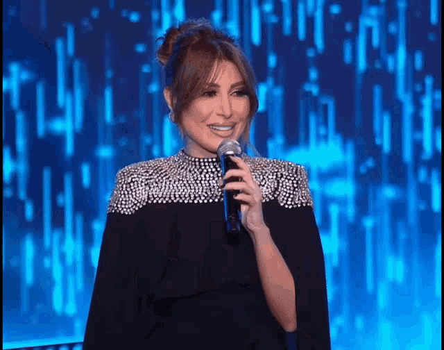 a woman in a black cape is holding a microphone and smiling