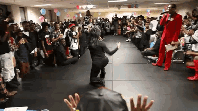 a man in a red suit stands in front of a crowd while a woman kneeling on the floor performs
