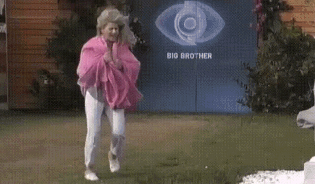 a woman in a pink blanket is standing in front of a big brother sign