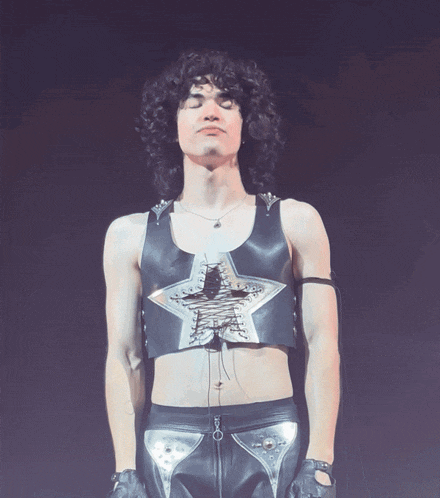 a man with curly hair is wearing a black leather vest with a silver star on it