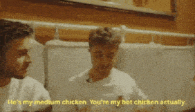 two men are sitting next to each other in a restaurant and one of them is eating chicken .