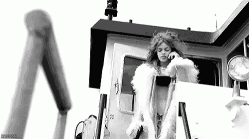 a woman in a white fur coat is talking on a cell phone in a black and white photo .