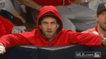 a man wearing a red hoodie is sitting in a stadium with mlb.com in the background