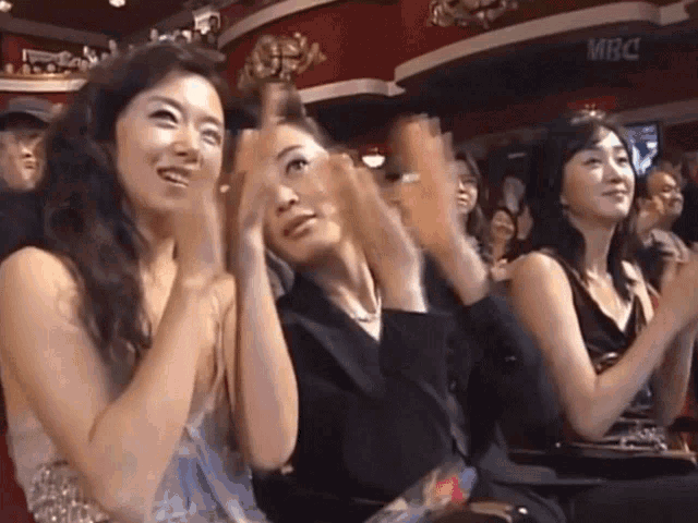 a group of women applauding in front of a sign that says mbc on it