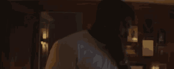 a man in a white shirt is standing in a dark room talking on a phone .