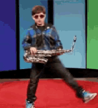 a young boy wearing sunglasses is holding a saxophone on a red carpet