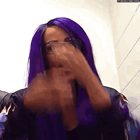 a woman with purple hair is covering her mouth with her hands .