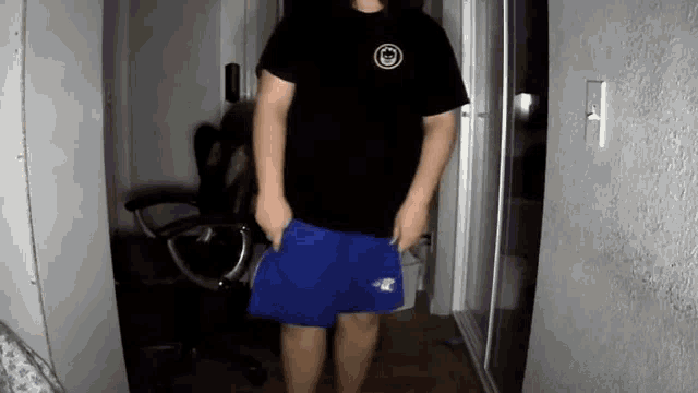 a man in a black t-shirt and blue shorts is standing in a hallway .
