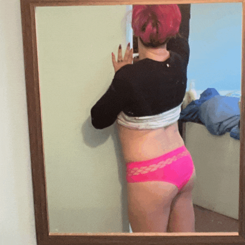 a woman with pink hair is taking a selfie in a mirror