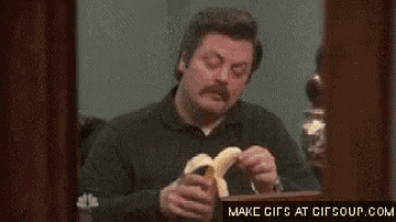 a man with a mustache is eating a banana at a table .