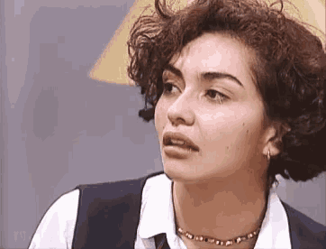 a woman with curly hair is wearing a choker and a vest .
