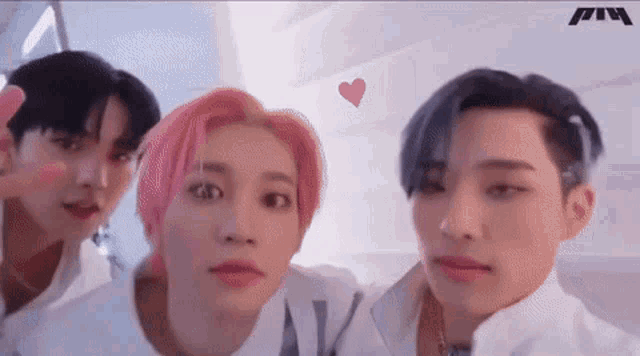 a group of three young men are posing for a picture together and one of them has pink hair .