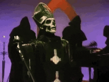 a skeleton in a priest 's robe is holding a microphone in front of a group of people .