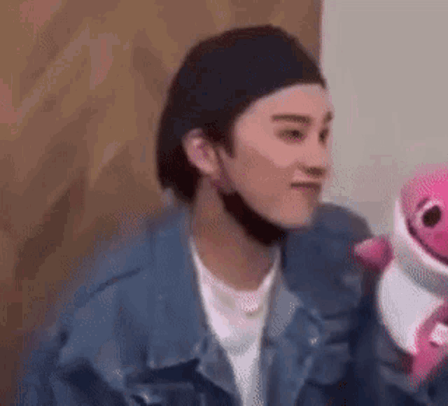 a man in a denim jacket is holding a pink stuffed animal .