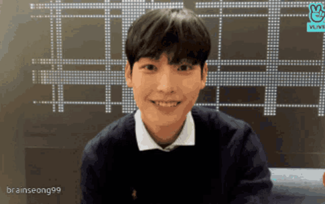 a young man smiles in front of a vlive screen