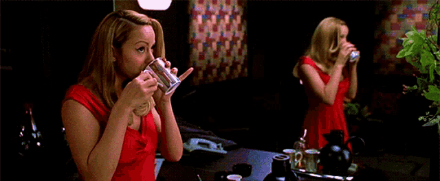 a woman in a red dress is drinking a cup of coffee in front of a mirror