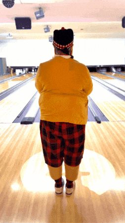 a man in a yellow sweater and plaid shorts is standing in front of a bowling alley