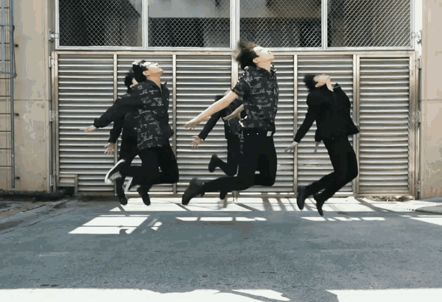 a group of people jumping in the air in front of a fence